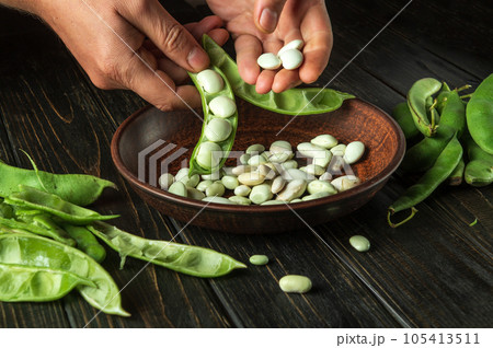 Cleaning bean seeds from green pods by the hands of a cook after harvesting. Work environment on the kitchen table. Cleaning bean seeds from green pods by the hands of a cook after harvesting. Work environment on the kitchen table. 105413511