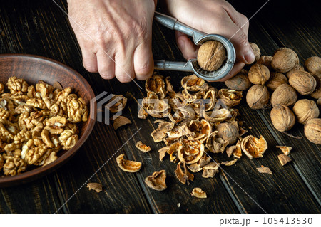 Peeling nuts with a nutcracker by human hands. Peeled walnuts in a plate and on the kitchen table Peeling nuts with a nutcracker by human hands. Peeled walnuts in a plate and on the kitchen table 105413530