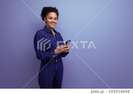 charming slender young hispanic brunette woman with fluffy curly hair in a blue denim suit holds a charming slender young hispanic brunette woman with fluffy curly hair in a blue denim suit holds a 105414698