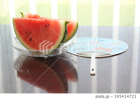 皿に入れられた二切れのすいかと傍らにうちわ 105414721