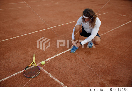 High angel view on young male tennis player tying shoelaces on court High angel view on young male tennis player tying shoelaces on court 105417590