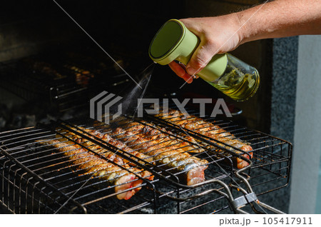 Male hand watered with olive oil, spices fish, baked on a grill. Male hand watered with olive oil, spices fish, baked on a grill. 105417911