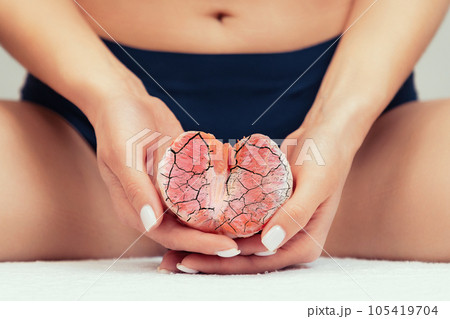 A woman holds half a grapefruit with cracks near the intimate area. Close-up. The concept of gynecological problems A woman holds half a grapefruit with cracks near the intimate area. Close-up. The concept of gynecological problems 105419704