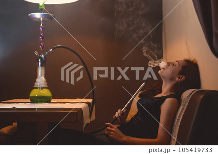 A young woman relaxing on the couch Smoking a hookah 105419733
