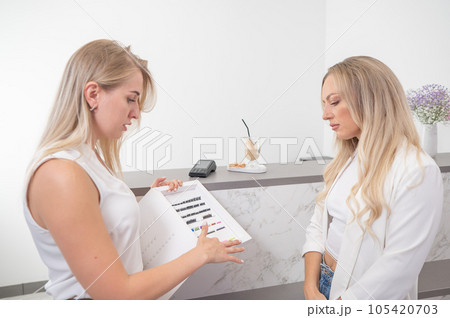 Eyelash extension master shows examples to a client. Woman choosing type of eyelash extension. Eyelash extension master shows examples to a client. Woman choosing type of eyelash extension. 105420703