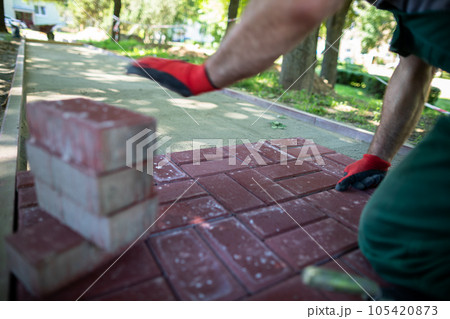 A construction worker kneels to lay paving stones on a sunny day. 105420873