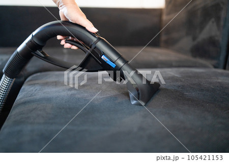 Cleaning service company employee removing dirt from furniture in flat with professional equipment. Female housekeeper arm cleaning sofa with washing vacuum cleaner close up 105421153