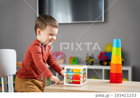 A cute little toddler boy of two years old plays with multi-colored balls and sits at a children's table in his room. Tactile sensory balls. Educational toys for children. Soft selective focus 105421253