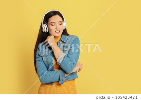 Young woman listening to audiobook on yellow background. Space for text 105423421