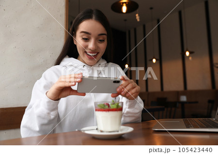 Young blogger taking picture of dessert at table in cafe Young blogger taking picture of dessert at table in cafe 105423440