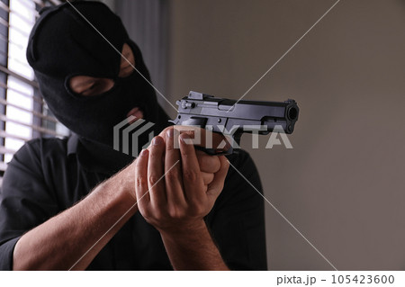 Man in mask holding gun indoors, focus on hands Man in mask holding gun indoors, focus on hands 105423600