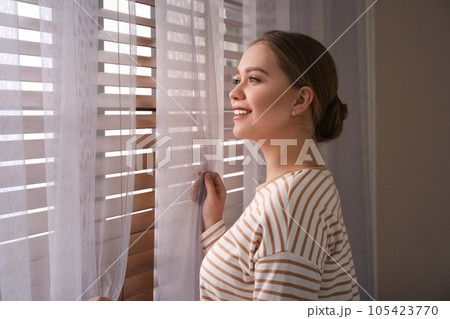 Woman near window with beautiful curtains at home Woman near window with beautiful curtains at home 105423770