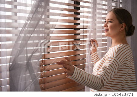 Woman opening window curtains at home in morning Woman opening window curtains at home in morning 105423771