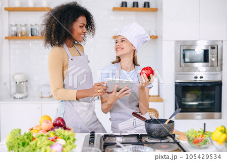 couple LGBT women friend holiday activity using tablet technology internet help learning cooking healthy food lovely cute together 105429534