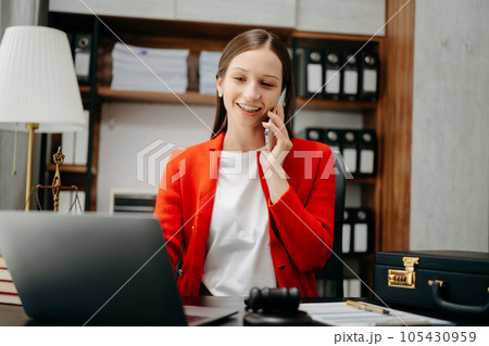 Caucasian female lawyer chatting online with client on laptop, smartphone  discussing details of lawsuit. in office 105430959