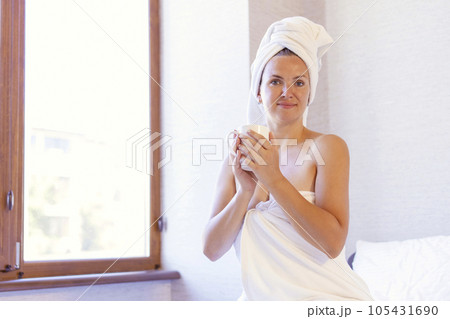 Woman in bath towel and towel on hair holding a cup and smiling 105431690