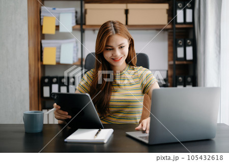Business asian woman Talking on the phone and using a laptop with a smile while sitting at home office. 105432618