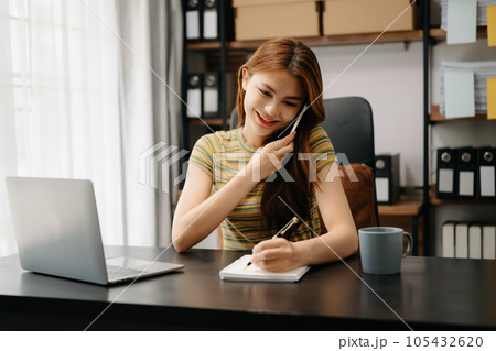 Business asian woman Talking on the phone and using a laptop with a smile while sitting at home office. 105432620
