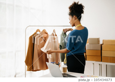 Calm curly brunette dark skinned woman on desk in modern office of fashion designer and holds tablet and smartphone. Calm curly brunette dark skinned woman on desk in modern office of fashion designer and holds tablet and smartphone. 105434873