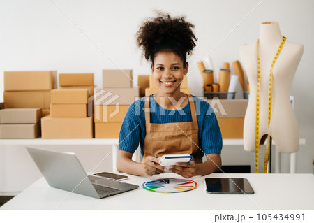Startup small business SME, Entrepreneur owner African woman using smartphone or tablet taking receive and checking online purchase shopping order to preparing pack product box. in office. Startup small business SME, Entrepreneur owner African woman using smartphone or tablet taking receive and checking online purchase shopping order to preparing pack product box. in office. 105434991