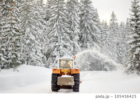 A snowplow truck clearing a snow-covered road in the European Alps while a snowstorm. Drifts and snow drifts during a snowfall. 105436425