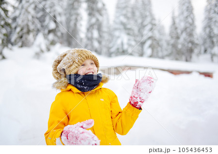 Happy preteen boy having fun playing with fresh snow during vacation in european Alps. Child dressed in warm clothes, hat, hand gloves and scarf. Happy preteen boy having fun playing with fresh snow during vacation in european Alps. Child dressed in warm clothes, hat, hand gloves and scarf. 105436453