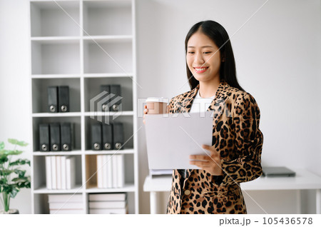 Young attractive Asian female office worker business suits smiling at camera with working notepad, tablet and laptop documents . in office Young attractive Asian female office worker business suits smiling at camera with working notepad, tablet and laptop documents . in office 105436578