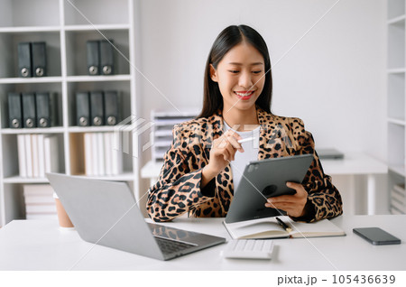 Successful Asian Businesswoman Analyzing Finance on Tablet and Laptop at Office Desk tax, report, accounting, statistics, and analytical research concept. Successful Asian Businesswoman Analyzing Finance on Tablet and Laptop at Office Desk tax, report, accounting, statistics, and analytical research concept. 105436639