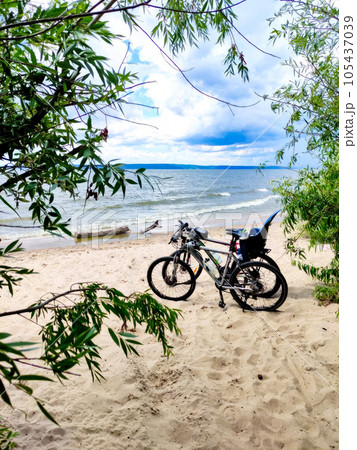 Two mountain bikes on a sandy beach. Blue sky, white clouds and green trees. Two mountain bikes on a sandy beach. Blue sky, white clouds and green trees. 105437039