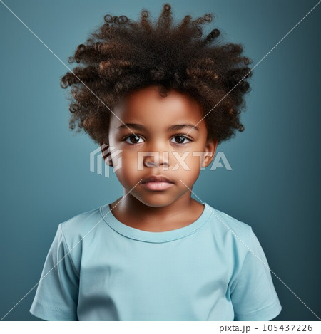 Portrait of a little African boy with brown curly hair. Closeup face of a serious African American child on a blue background looking at the camera. Front view of an unsmiling kid in a blue shirt. 105437226