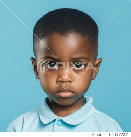 Portrait of a little African boy with brown curly hair. Closeup face of a serious African American child on a blue background looking at the camera. Front view of an unsmiling kid in a blue shirt. 105437227