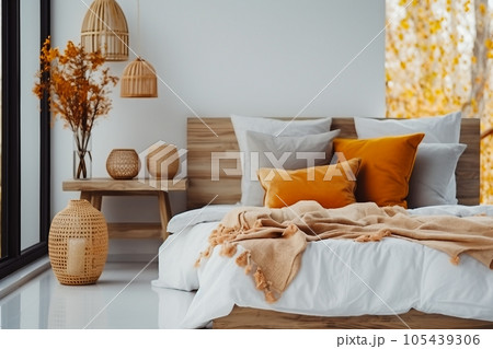 interior design, Brown and orange pillows on white bed in natural bedroom interior with wicker lamp and wooden bedside table with vase interior design, Brown and orange pillows on white bed in natural bedroom interior with wicker lamp and wooden bedside table with vase 105439306