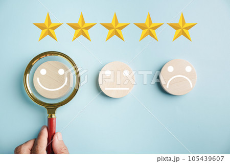 Magnifying glass held by hand selects happy smiley face icon among emotions. Good feedback rating, positive customer review. Experience, satisfaction survey. Certificate represents satisfaction. 105439607
