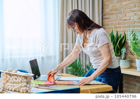 Mature woman interior designer working at her desk with fabric samples, laptop Mature woman interior designer working at her desk with fabric samples, laptop 105440796