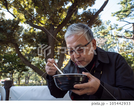 An older asian man eating noodles and soup with chopsticks 105442933