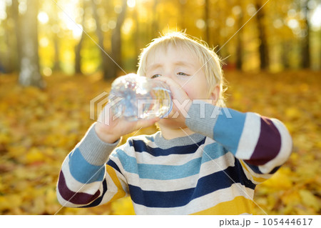 Little boy drinks water during walking at autumn in forest or park. Little boy drinks water during walking at autumn in forest or park. 105444617