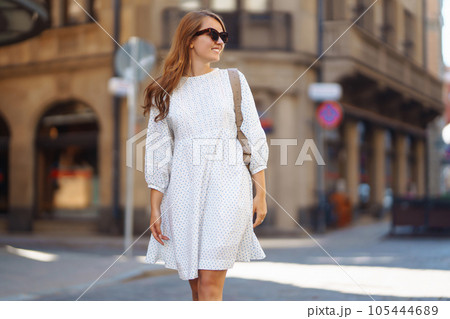 Young woman in white dress walks through streets of city. Lifestyle, travel and vacations concept Young woman in white dress walks through streets of city. Lifestyle, travel and vacations concept 105444689