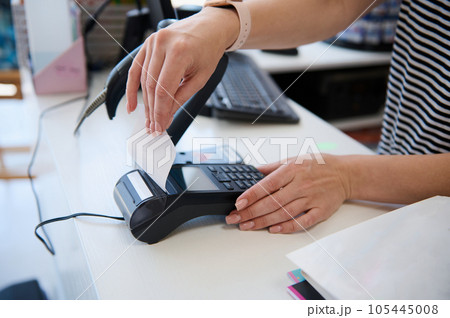 Close-up salesperson using POS terminal in a store, receiving a cashless payment and taking out a receipt for a purchase 105445008