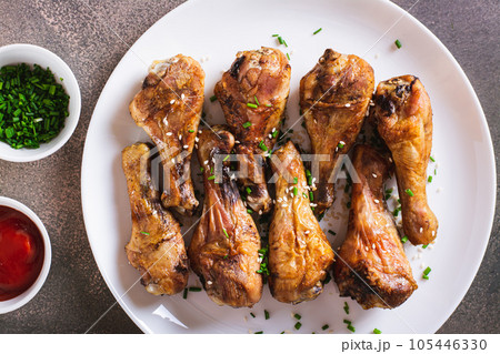 Closeup of baked chicken drumsticks with green onions and sesame seeds on a plate top view Closeup of baked chicken drumsticks with green onions and sesame seeds on a plate top view 105446330