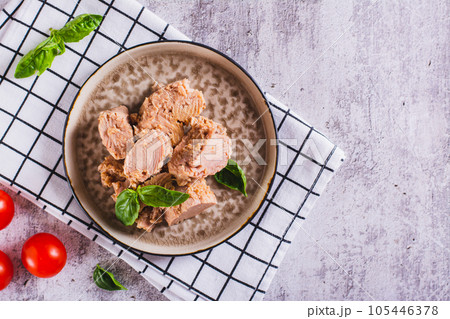 Pieces of canned tuna and basil leaves on a plate top view Pieces of canned tuna and basil leaves on a plate top view 105446378