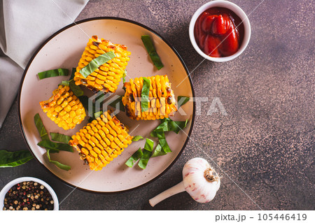 Baked sweet corn cobs with butter, garlic and herbs on a plate top view 105446419