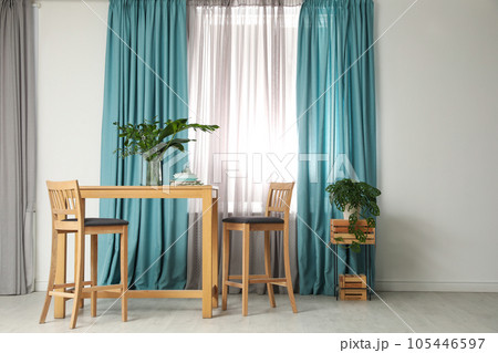 Stylish wooden table and chairs near window with elegant curtains in room Stylish wooden table and chairs near window with elegant curtains in room 105446597