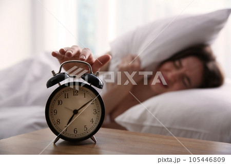 Young woman turning off alarm clock at home in morning, focus on hand Young woman turning off alarm clock at home in morning, focus on hand 105446809