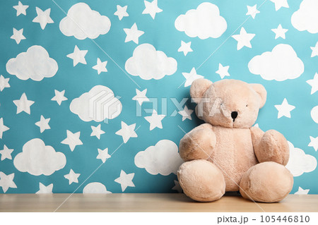 Teddy bear on wooden table near wall with painted blue sky, space for text. Baby room interior Teddy bear on wooden table near wall with painted blue sky, space for text. Baby room interior 105446810