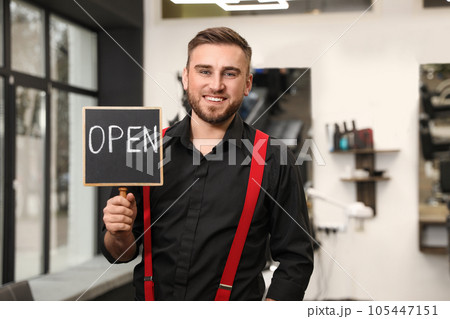Young business owner holding OPEN sign in his barber shop 105447151
