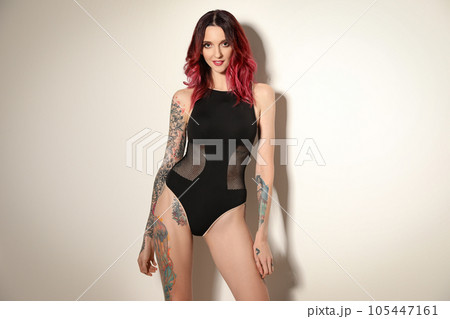 Beautiful woman with tattoos on body against light background 105447161