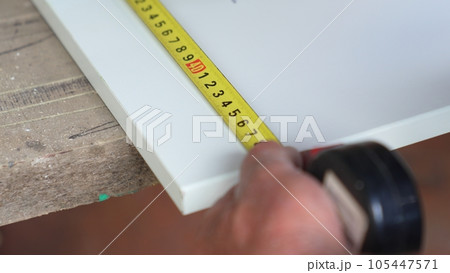 Men's hands take measurements and apply cut lines to chipboard.  105447571