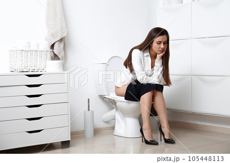 Upset woman sitting on toilet bowl in bathroom 105448113