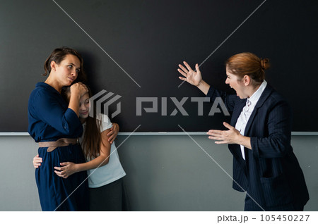 The teacher screams at the schoolgirl and her mother standing at the blackboard.  105450227