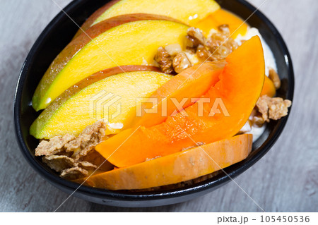 Mango slices and baked pumpkin with yogurt, cereals, nuts 105450536